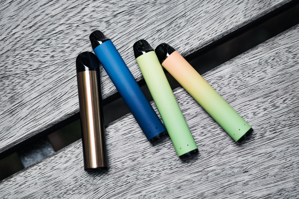 Four disposable vapes on a wooden bench