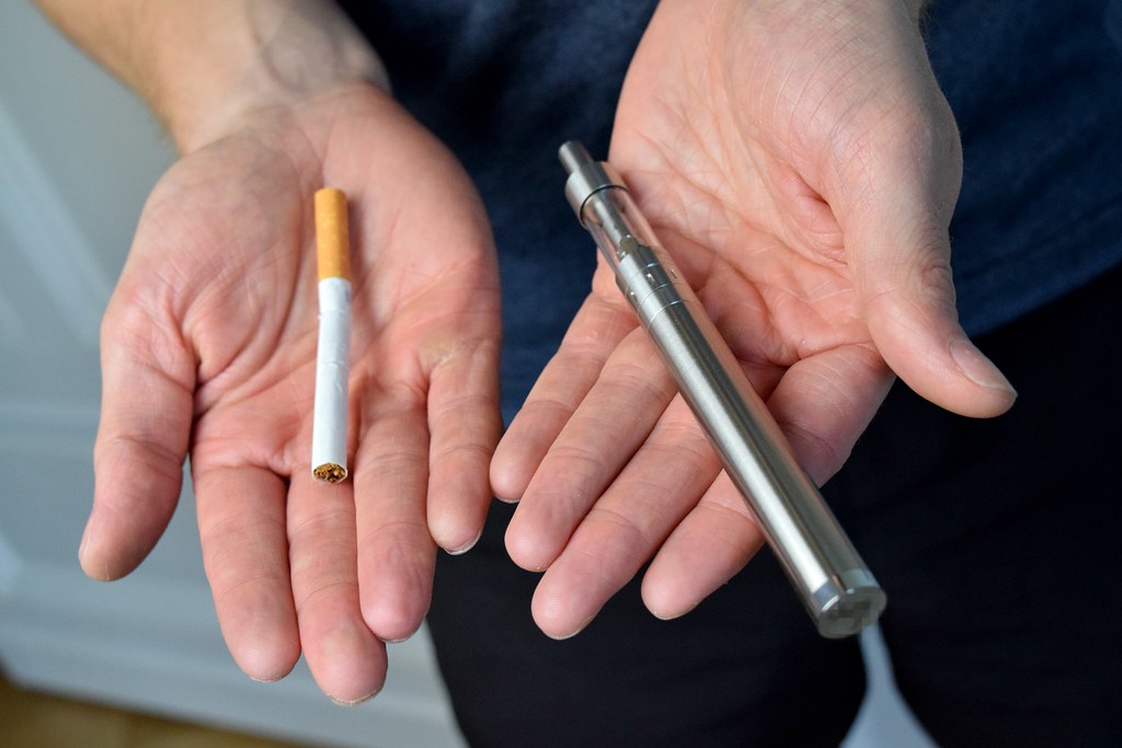 Hands holding a cigarette and an e-cigarette side by side